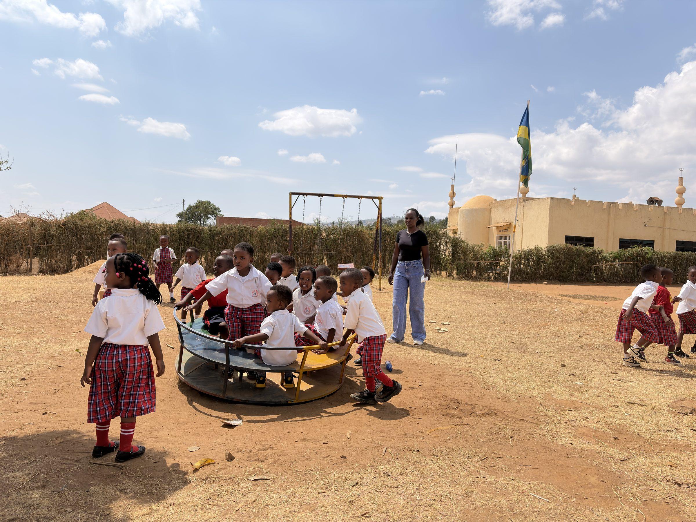Children on a roundabout in the earth yard, the Rwandan flag flying behind them