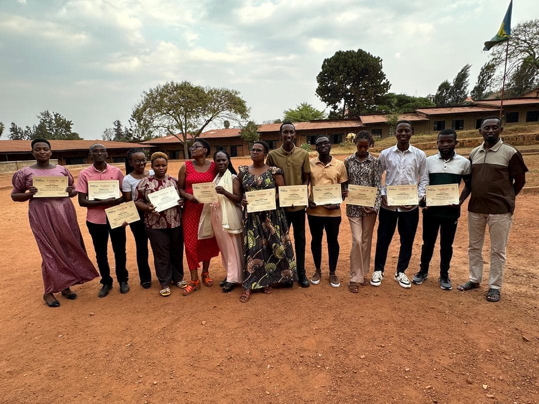 A row of adults holding certificates in front of the school buildings