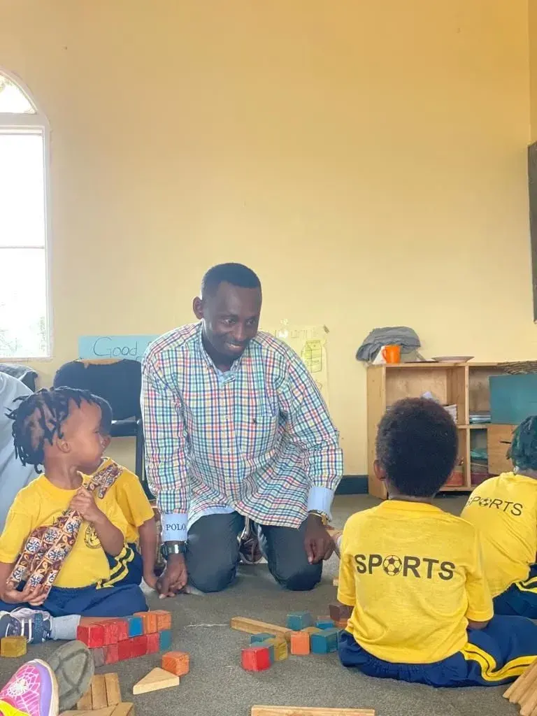 Eddy Kalisa Nyarwaya kneeling among young children building with wooden blocks