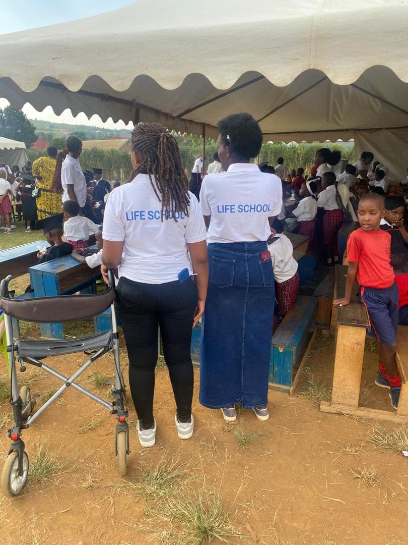 Two staff members in Life School shirts watching over children under an event tent