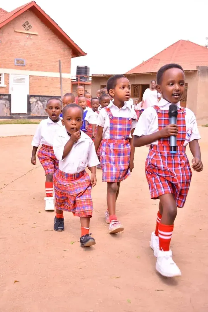 Young children in checked uniforms marching across the school yard