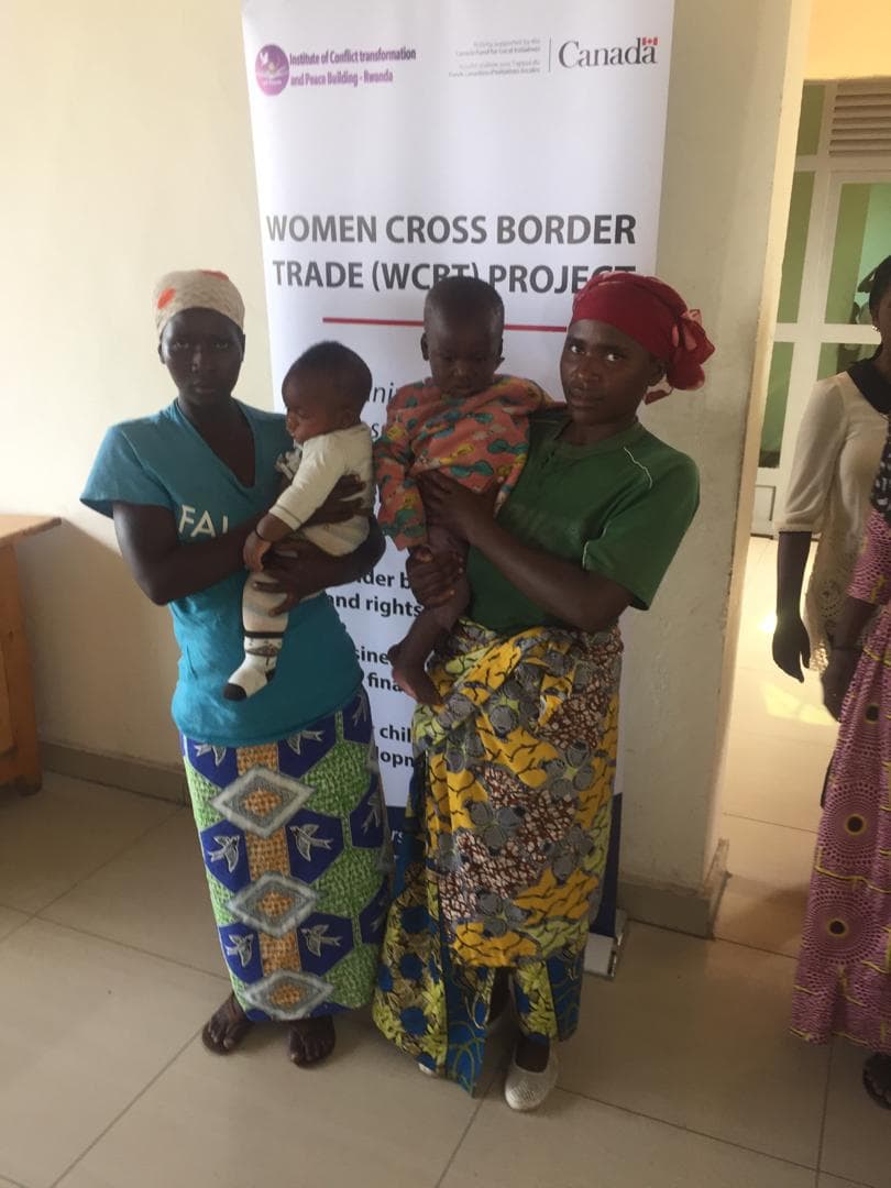 Two cross-border trader women holding their babies in front of a project banner