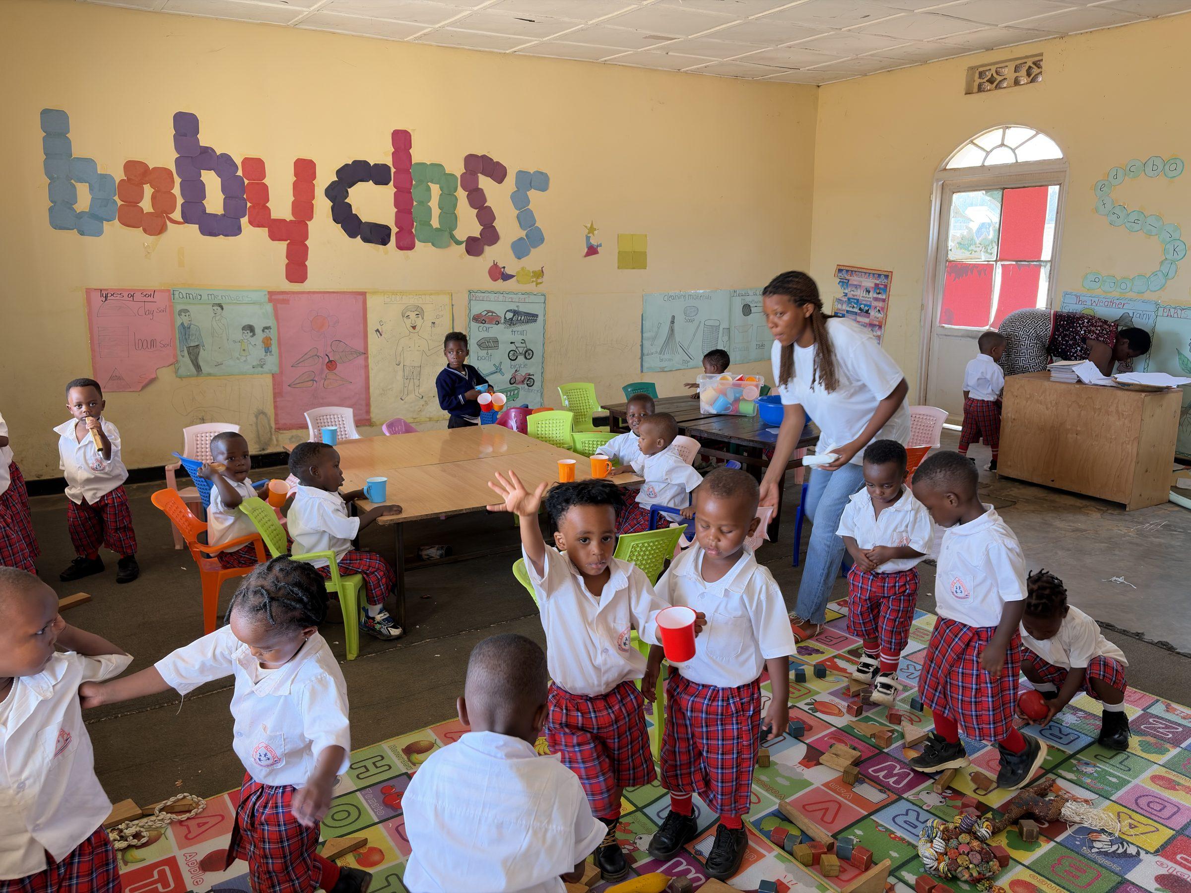 The youngest children at a table, the words baby class painted on the wall behind them