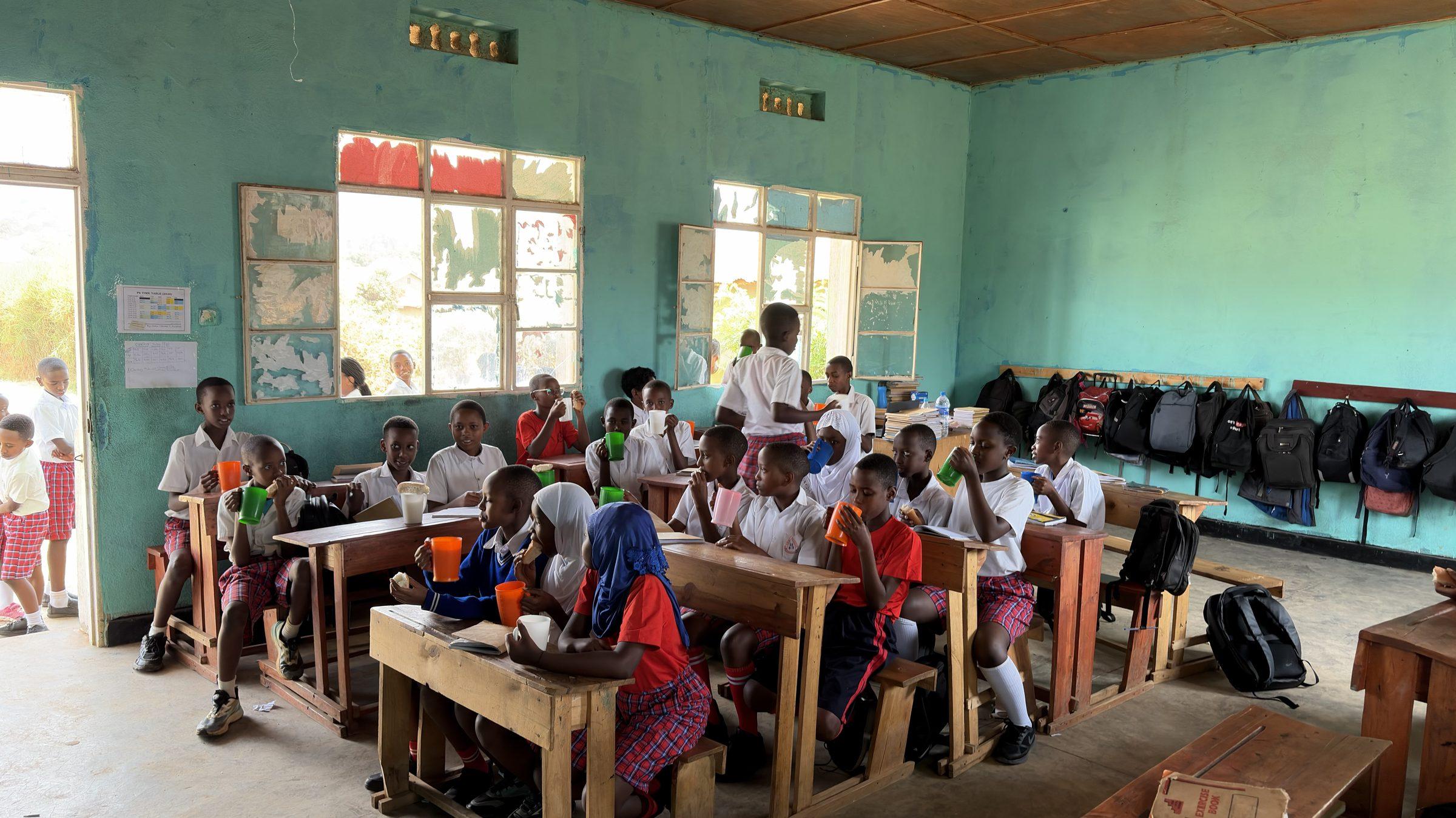 Pupils eating breakfast from bowls at their desks, a teacher at the front