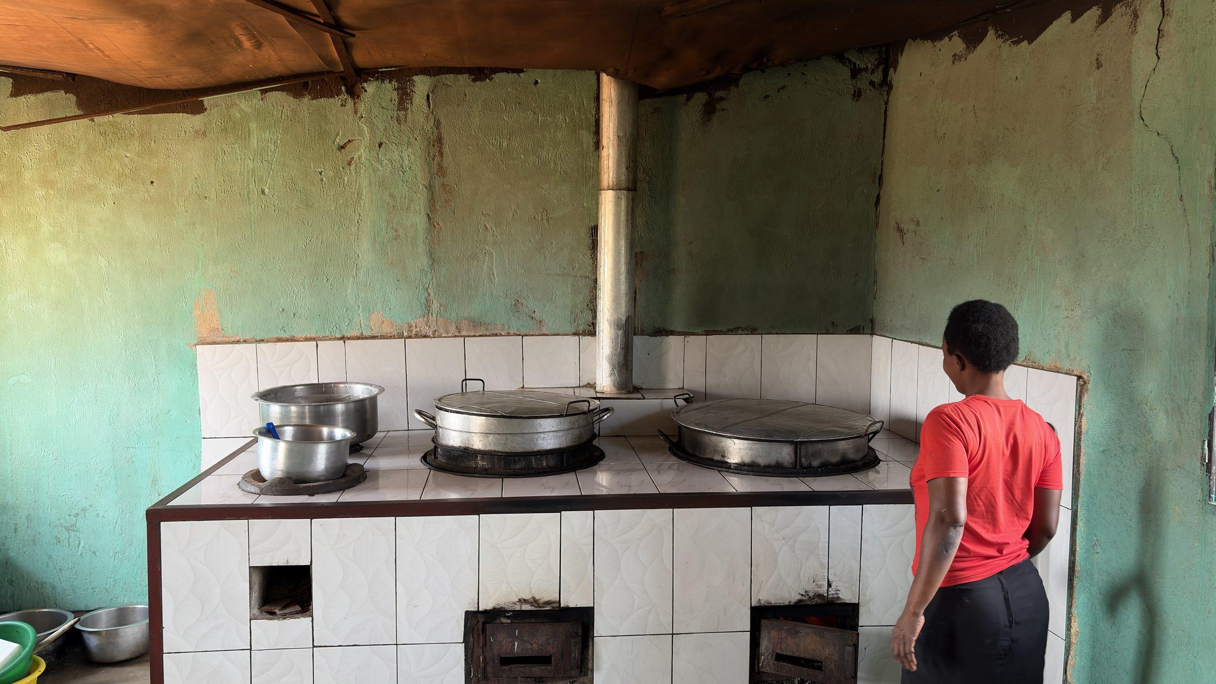 Large cooking pots on a tiled stove, a staff member standing at the wall