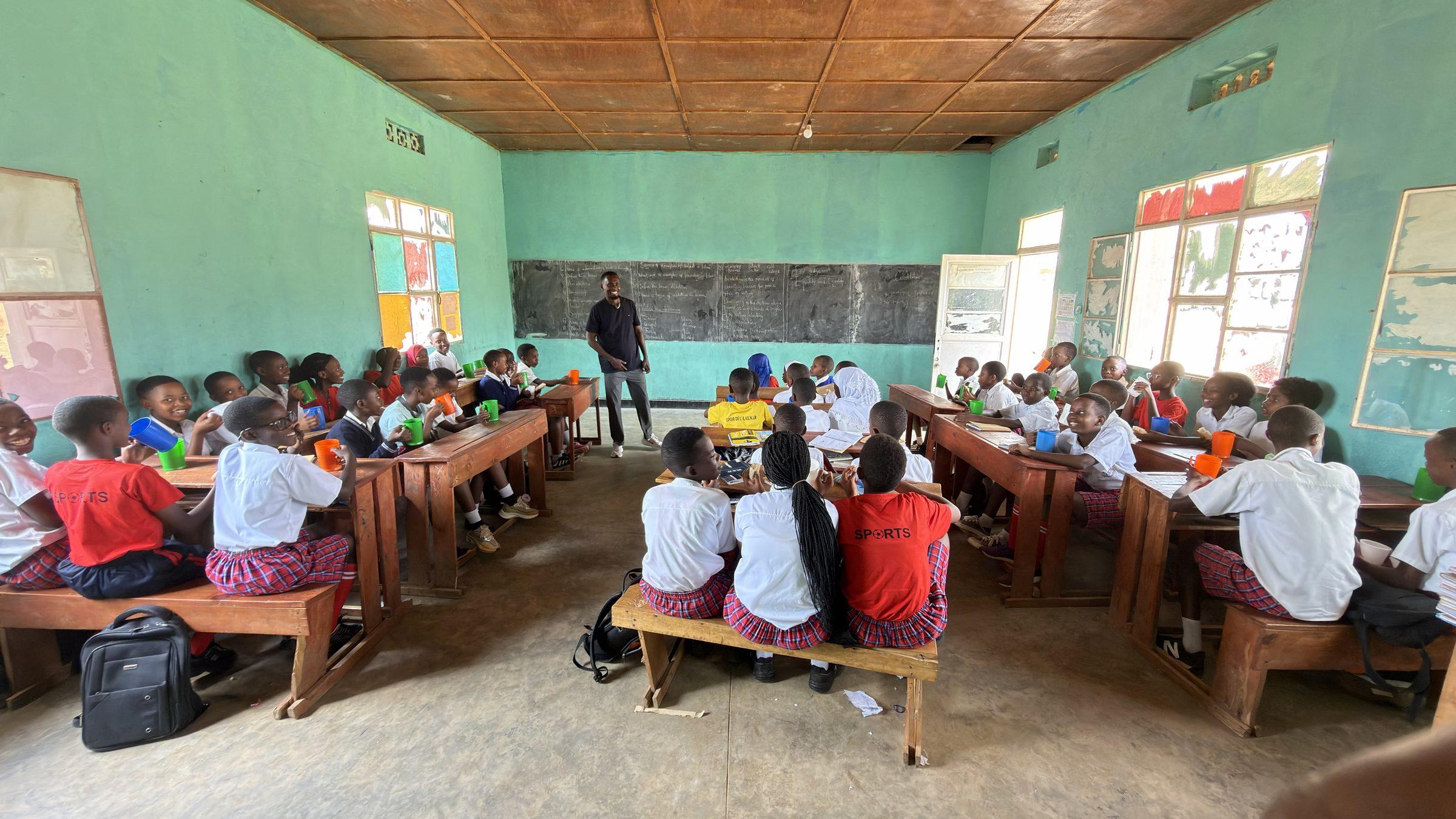 Pupils in red sweaters eating at long desks, the chalkboard behind