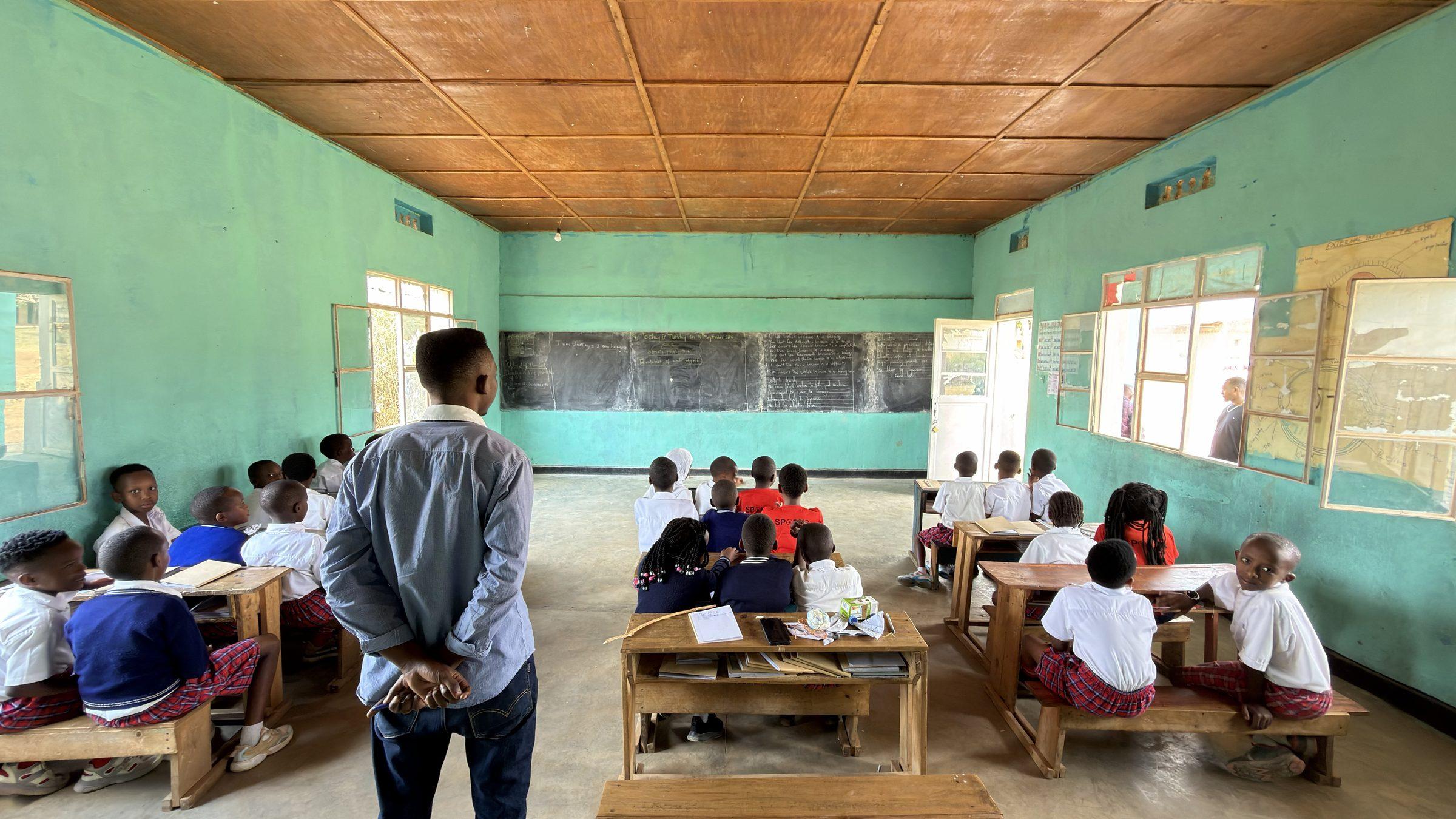 A teacher at the front of the class, pupils at desks seen from behind