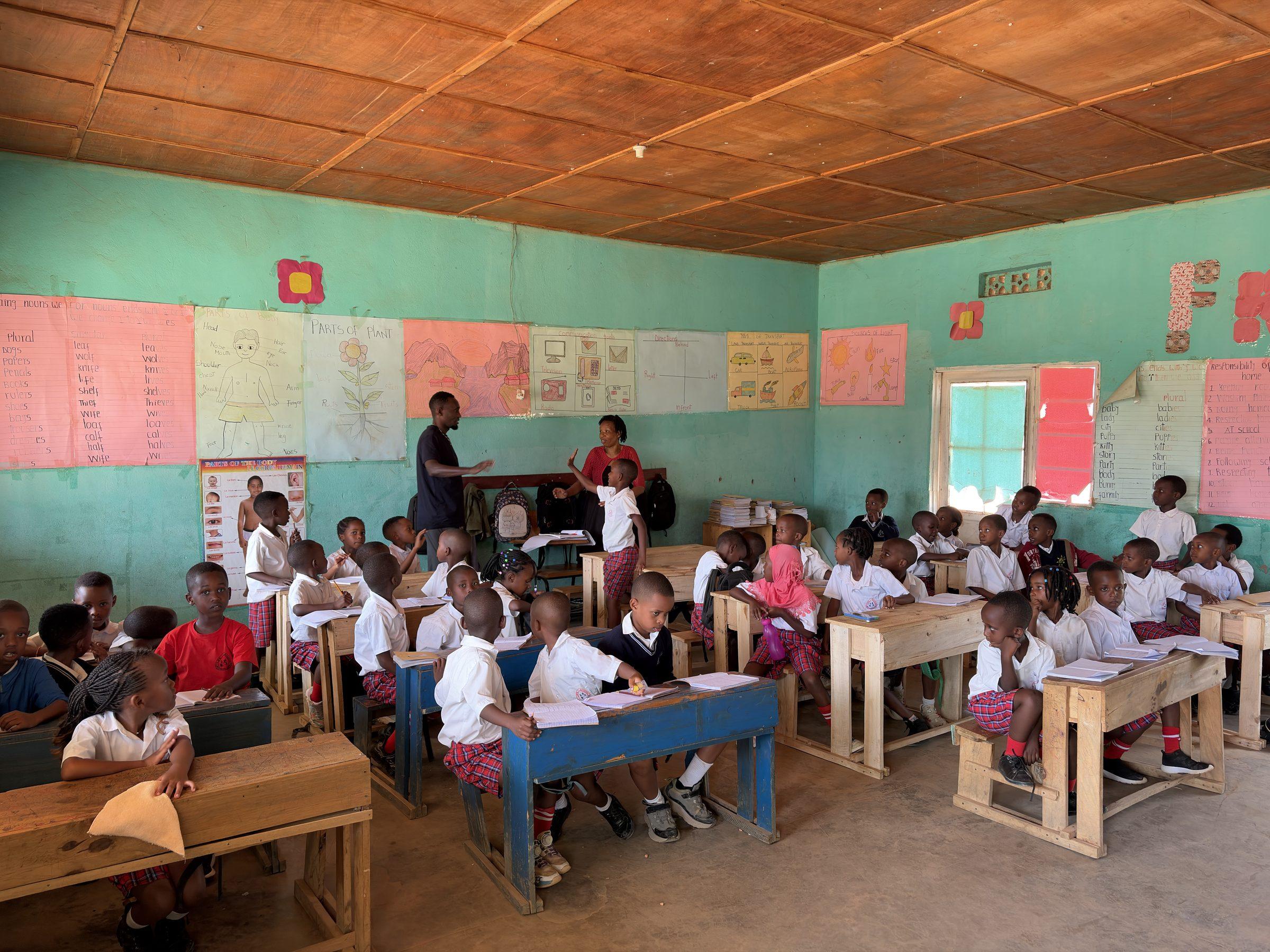Pupils in white shirts at desks, a teacher at the front, charts on the wall