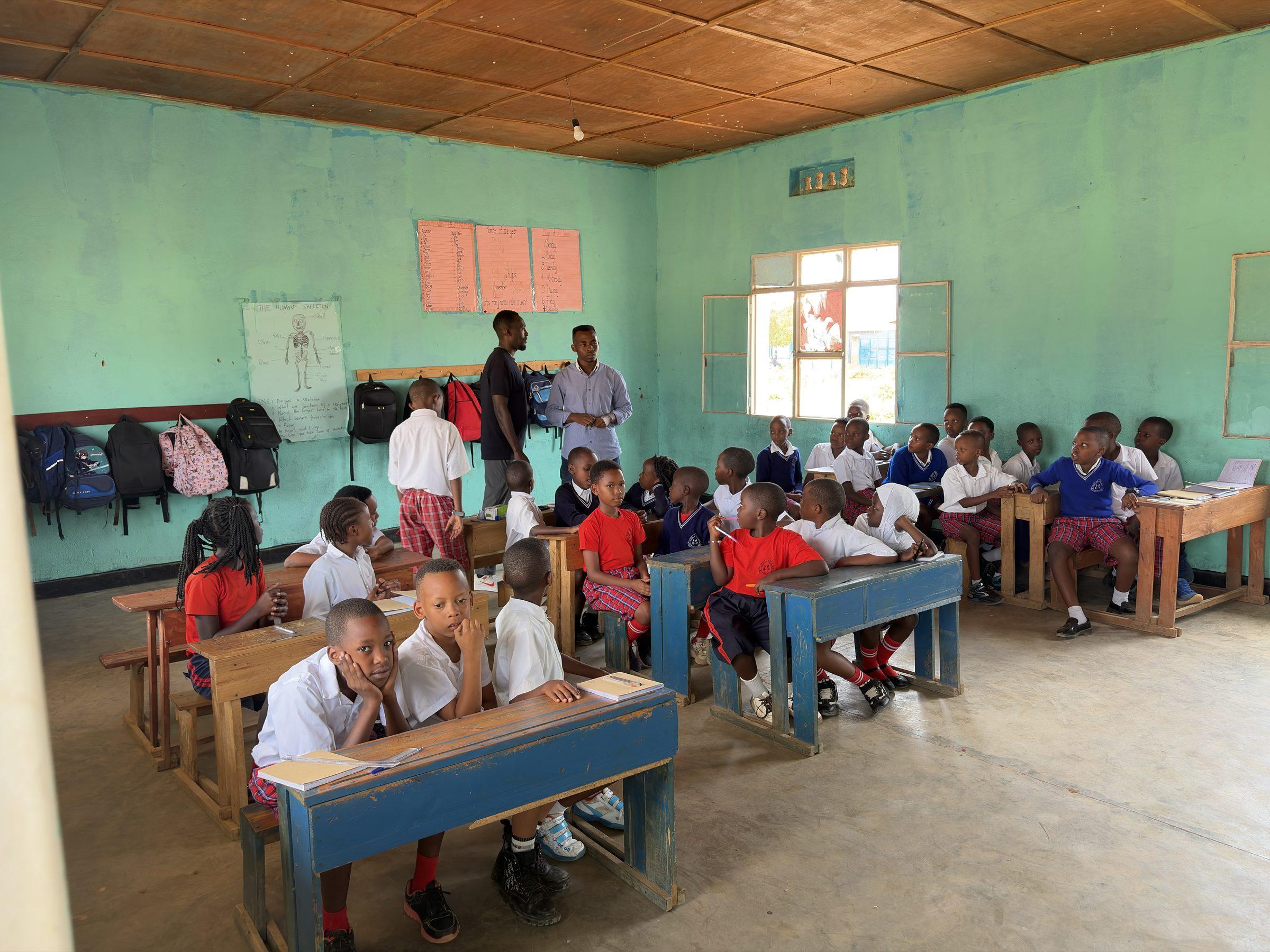 Pupils in red sweaters and white shirts at desks, a teacher standing at the side