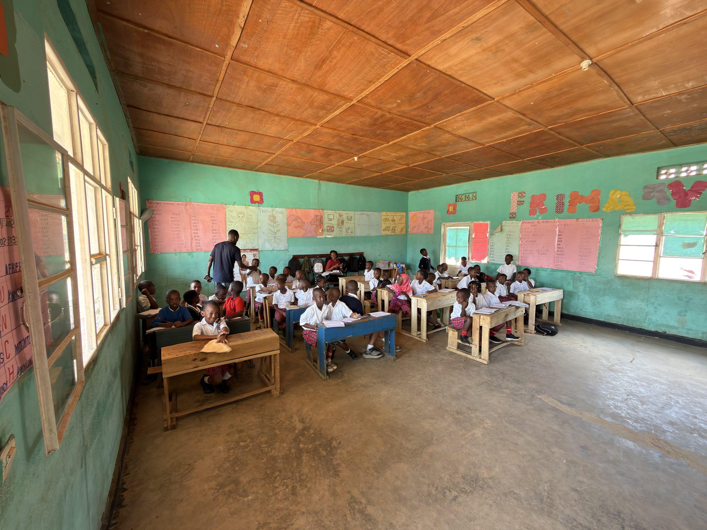 Pupils at desks in a wide classroom with a timber ceiling and a chalkboard