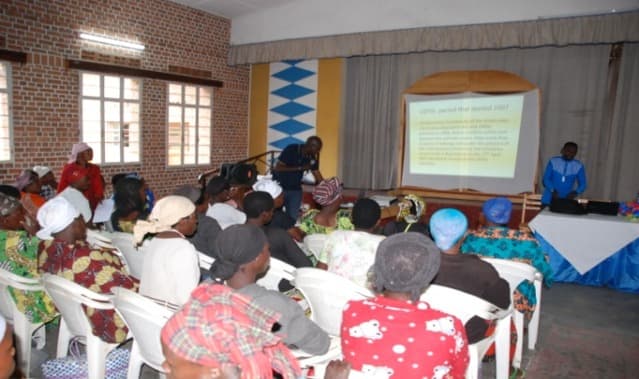 Women seated in a hall facing a facilitator and a projected presentation
