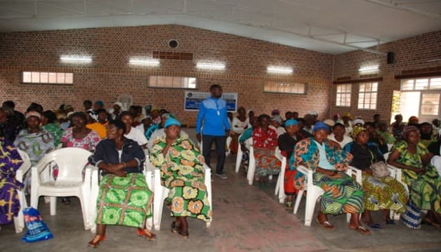 Rows of women seated on plastic chairs in a brick hall during a training